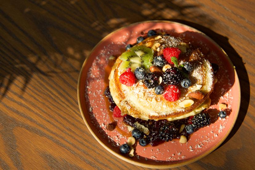 Fluffy buttermilk pancakes on blueberry jam served with seasonal fruits, nuts, coconut flakes, maple syrup, and vanilla ice cream.