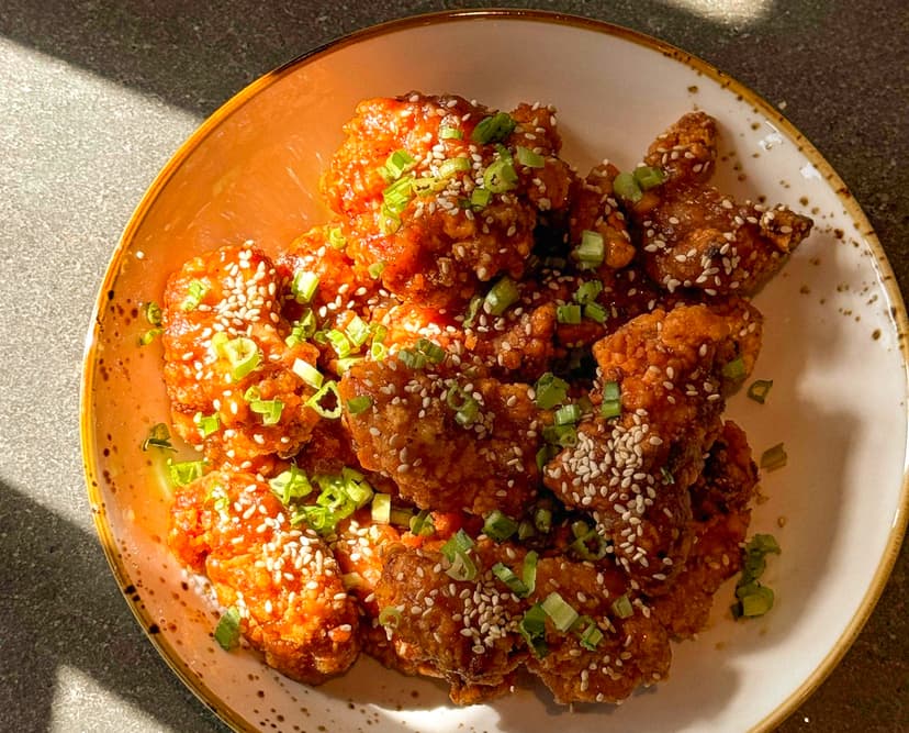 Buttermilk fried chicken with homemade honey garlic sauce, sesame seeds, green onions, saw leaves.